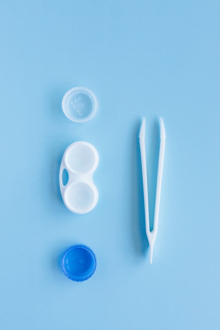 programs-01 A contact lens kit featuring a lens case and tweezers arranged on a blue background in flat lay style.