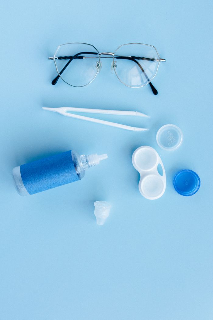 programs-02 Flat lay of eye care essentials including glasses and contact lens solution on a blue background.