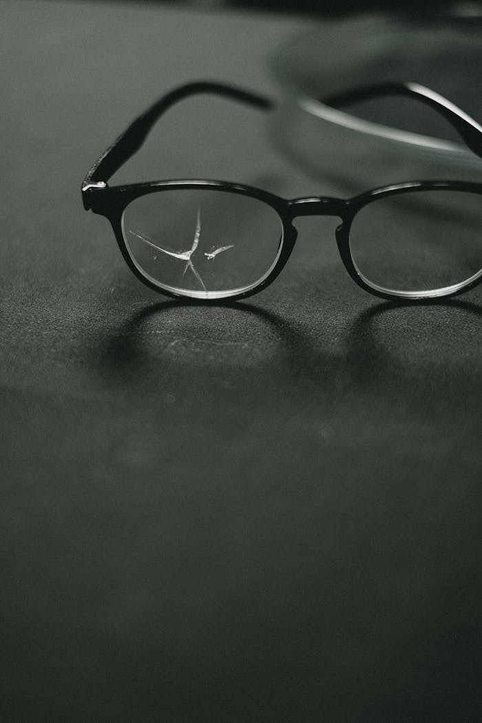 Close-up of broken eyeglasses on a gray surface, indoors with defocused background.